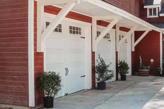 Classic Barn Charm A red building with three white garage doors and potted plants at the entrance.