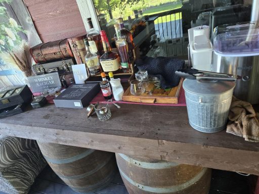 Whiskey & Cigar Bar A rustic bar setup featuring various bottles, glasses, and a wooden countertop.