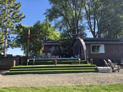 Ceremony Ready A house with a landscaped yard, seating area, and a large wooden cross visible.
