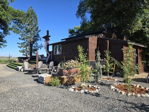 Gathering Under the Pines A rustic brick house with garden decorations and outdoor seating among greenery.