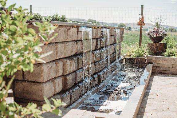 Garden Water Wall A serene waterfall cascading over stone blocks in a landscaped outdoor setting.