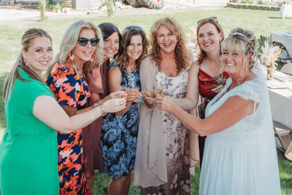 Bridesmaids' Toast A group of seven women celebrating together, holding drinks in a sunny outdoor setting.